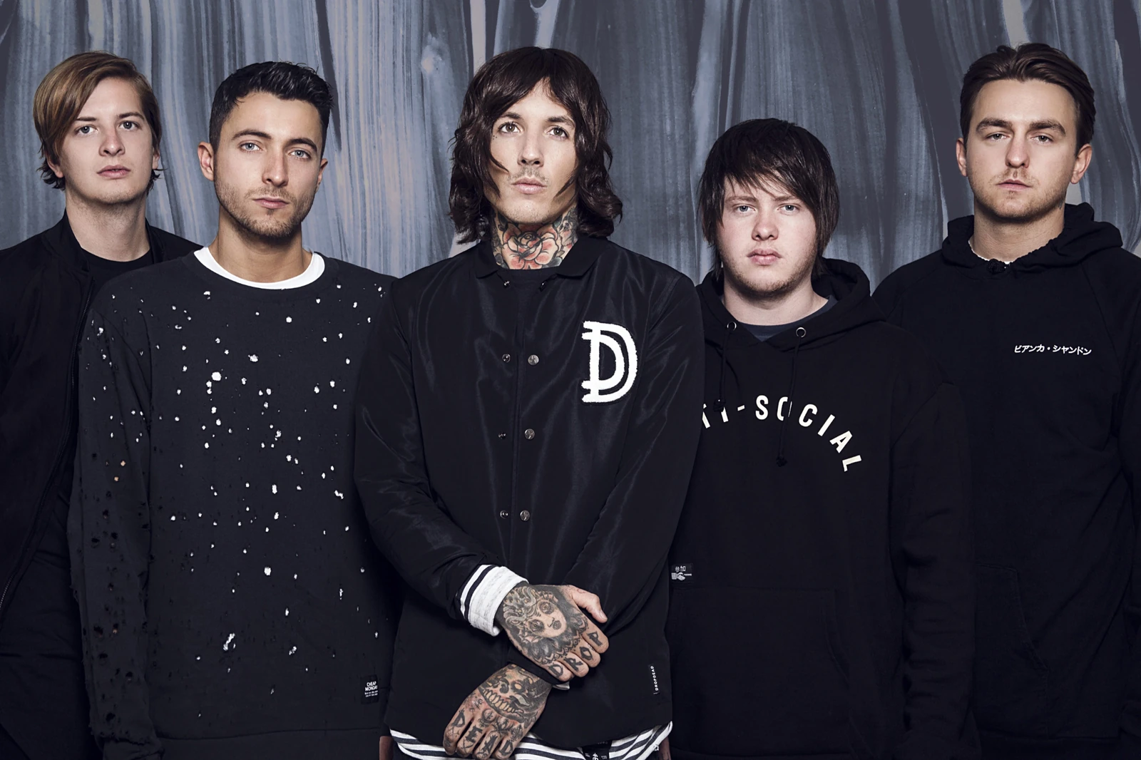 Photo de groupe de Bring Me The Horizon devant un rideau gris.