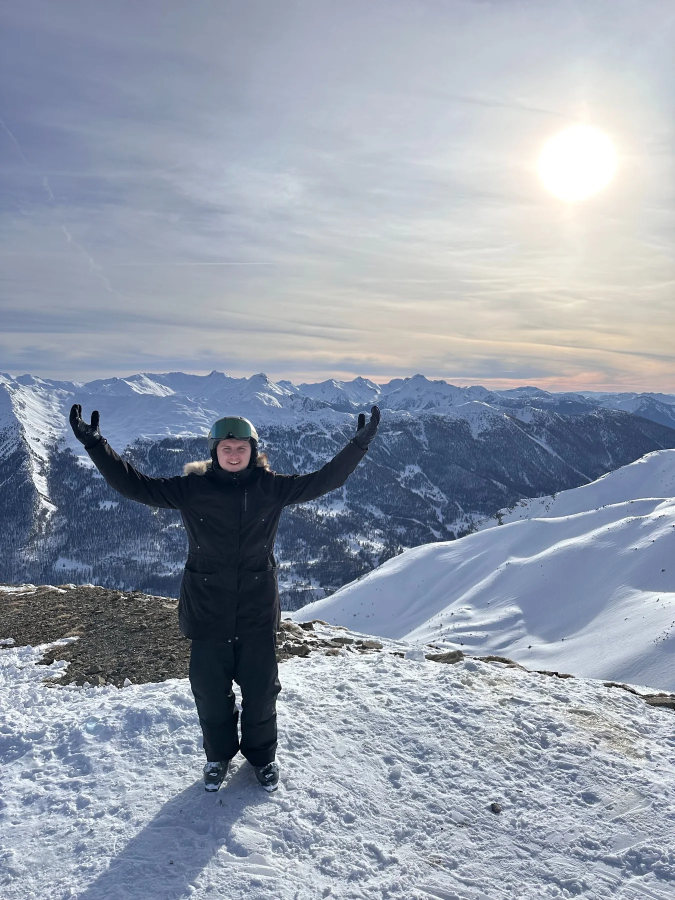 Nicolas au ski, les bras levés devant un panorama de montagnes enneigées.
